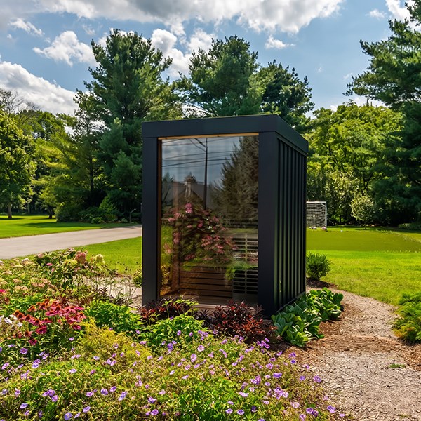 Neptune Mini Sauna with black metal siding and a large bronze glass front wall in a garden setting.